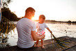 © Andriy Medvediuk - Young father and little son sitting on the wooden pier near the lake, at sunset on summer day. father's day