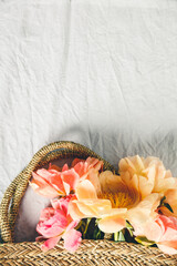 Wall Mural - flat-lay of beautiful peony flowers in straw bag over grey linen table cloth background