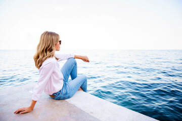 Wall Mural - Relaxed woman sitting on cliff and watching the blue ocean