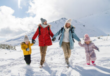 Father And Mother With Two Small Children In Winter Nature, Walking In The Snow.