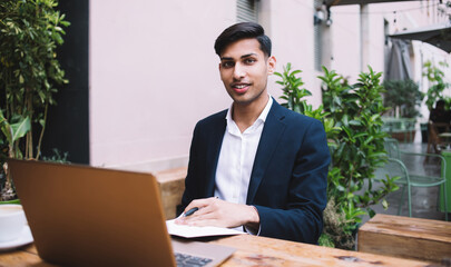 Friendly young man in suit working on laptop in cafe on open air