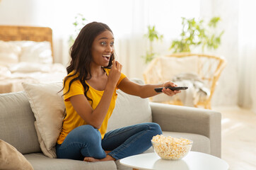 Wall Mural - Pretty African American lady with TV controller enjoying interesting movie at home, blank space