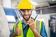 © winnievinzence - Portrait of male worker talking on radio phone or walkie-talkie with colleague to controlling work in front of industry machine at industrial factory. technology and communication at workplace