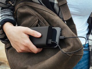 The girl uses a smartphone connected to the power Bank. Black smartphone and powerBank in women's hands close-up. Using gadgets in the modern world. The concept of portable chargers, modern tourism