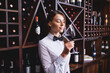 © LIGHTFIELD STUDIOS - Young sommelier smelling glass of wine near racks with bottles