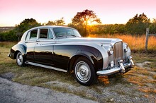 Front And Side View Of Classic, Vintage, Luxury, Two Toned Car At Sunset With Setting Sun Background On A Rural Road