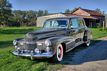 Front view of classic, vintage, luxury car in rural setting with whitewall tires, red wheels, chrome hubcaps, bumper, grill, fog lights, and rounded hood