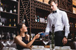 © LIGHTFIELD STUDIOS - Selective focus of young woman holding credit card near waiter in formal wear with payment terminal in restaurant