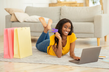 Wall Mural - Online shopping and delivery. Positive black woman with credit card and laptop ordering goods on web at home