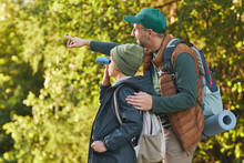 Portrait Of Happy Father And Son Hiking Together And Pointing Away While Walking In Forest With Backpack, Copy Space