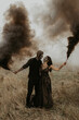 Couple with dark skull makeup with black smoke bombs in their hands.