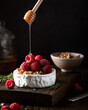 brie cheese with raspberries and walnuts pouring honey. Selective focus, dark background