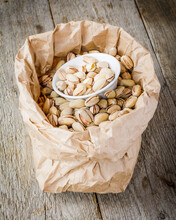 Pistachios In The Paper Bag On The Wooden Background
