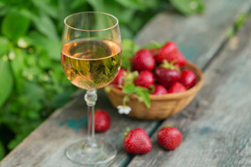 Wall Mural - Glass of rose wine served with fresh strawberries on wooden background. Picnic outdoor with pink wine and berries.