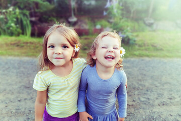 Portrait of two little cute smiling Caucasian girls with daisies in their hair. The concept of children's friendship and team. Retro toning.