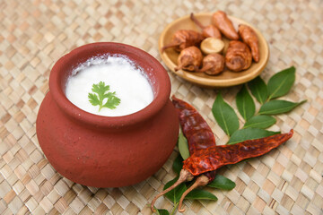 Wall Mural - Bowl of Indian homemade sour curd yogurt dahi fresh herbs in clay pot on a mat, Kerala, India. Indian Dairy product obtained by coagulating milk process called curdling. Its a probiotic food.