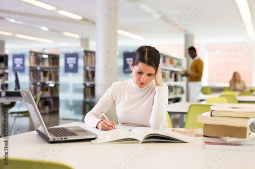 Portrait of upset tired female student preparing for exam in university library. High quality photo