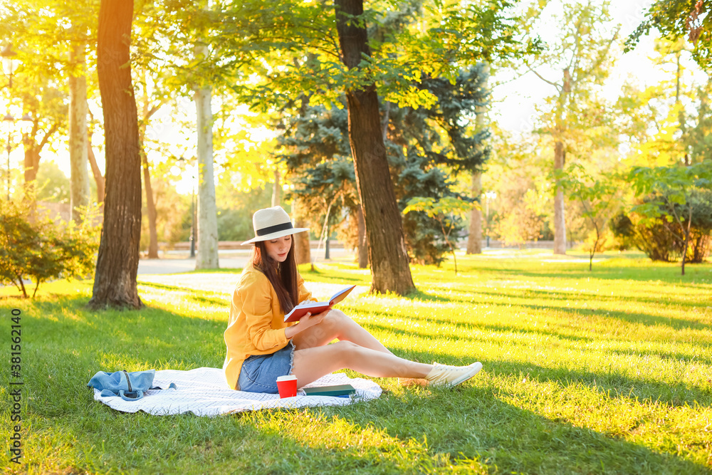 Beautiful young woman reading book in park