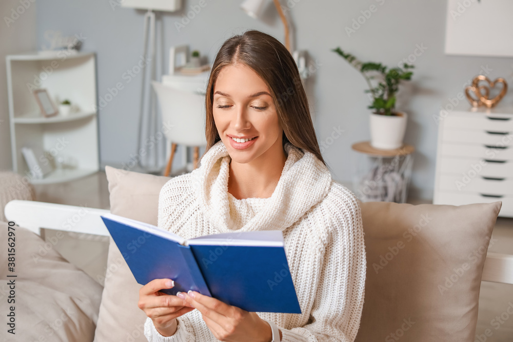 Beautiful young woman reading book at home