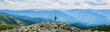 © anatoliy_gleb - Panorama mountain valley with green forests, rear view girl is sitting on guy shoulders with opening arms. Couple is standing on top of cliff, enjoying powerful view at scenery mountains at cloudy day