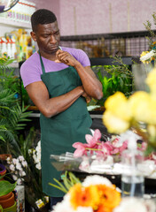 Portrait of pensive African American man florist thinking over creating of flower arrangement in shop..