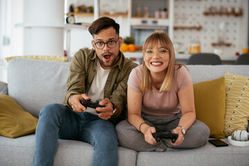 Wall Mural - Boyfriend and girlfriend playing video game with joysticks in living room. Loving couple are playing video games at home...