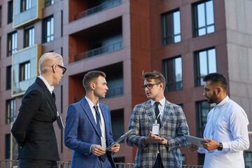 Wall Mural - Group of business colleagues discussing business project together during meeting in the city with modern building in the background