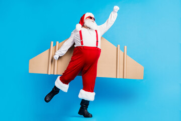 Wall Mural - Full length photo of stylish modern white grey hair bearded santa claus fly craft wings 0on x-mas christmas time noel night wear red costume isolated blue color background