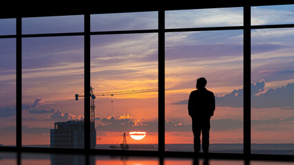 Wall Mural - The man standing near the panoramic window against the city sunset