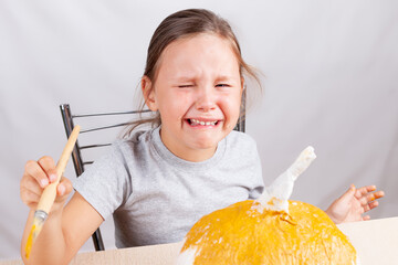 a girl cries and makes a handmade papier-mache pumpkin for Halloween on a gray background,.