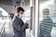 © Sanja - A young businessman with a mask puts on another glove, stands in front of cash machine, life during a pandemic caused by a virus