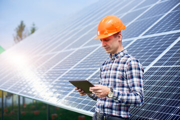 Wall Mural - Engineer in a helmet with a tablet in his hands near the solar panels station with a reflection of the sun in them. Home construction. Technology concept. Green ecological power energy generation