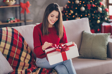 Wall Mural - Photo of positive girl sit couch open x-mas gift box wear red sweater in house indoors with x-mas atmosphere ornament