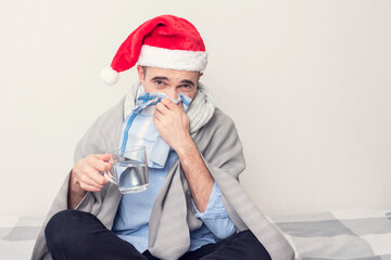 Santa with a handkerchief and a glass of water is ill with the flu, a man is sitting at home on self-isolation, portrait, white background