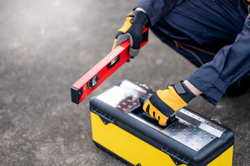 Male mechanic or maintenance worker man holding red aluminium spirit level tool or bubble levels and working tool box at construction site. Equipment for civil engineering project