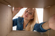 © Plutmaverick - Young beautiful girl blonde, opens and peeks into a cardboard box. To get or to put things to move, bottom view.