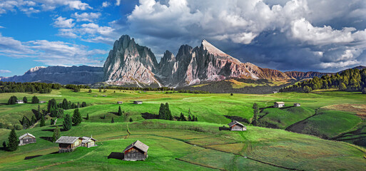 Wall Mural - Famous Alpe di Siusi - Seiser Alm with Sassolungo - Langkofel mountain group in background at sunset. Wooden chalets in Dolomites, Trentino Alto Adige region, South Tyrol, Italy