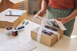 © AnnaStills - Close-up of woman decorating cardboard box with ribbon at the table before delivery