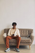 © AnnaStills - African young man sitting on sofa with mobile phone and credit card doing shopping online at home