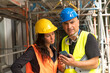 © cineberg - Senior engineer with his young trainee on construction site wearing safety vest, helmet and goggles checking the work plans on a smartphone