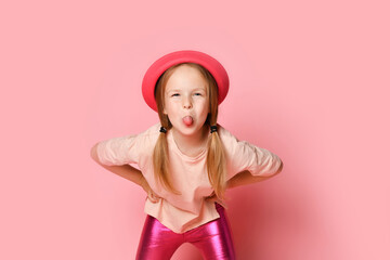 Mischievous little girl leaning forward with hands on hips and lolling while teasing or trolling someone. Close up shot isolated on pink