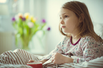 Cute little child girl ill sitting with tea in bed under blancket