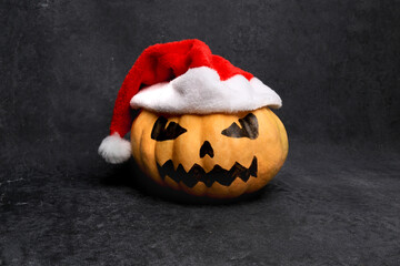 big orange ripe pumpkin with painted scary mystical face wearing santa claus hat, halloween and christmas celebration, american holidays, black background, place for text