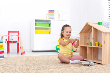 Wall Mural - Cute little playing with toys near wooden house on floor at home, space for text