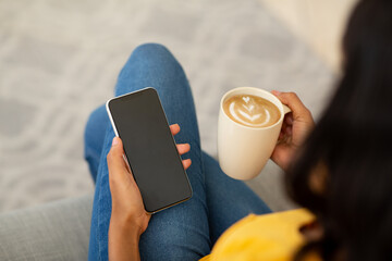 Wall Mural - Young black woman with coffee using smartphone to work or study online from home, space for mobile app design