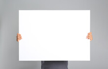 Man Holding White Blank Poster On Grey Background. Mockup For Design