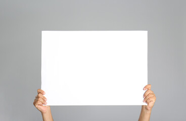Poster - Man holding white blank poster on grey background, closeup. Mockup for design