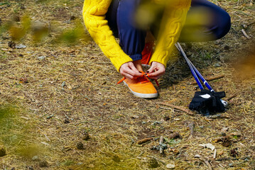 Wall Mural - Sporty hiking woman tying shoelaces on her jogging shoes while taking a break after hiking in autumn forest. hiking concept, outdoor lifestyle.