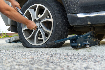 Wall Mural - Man changing wheel. tire changer changing flat car tire. Help on road concept. Mechanic hands unscrews a flat tire of a car raised on a jack