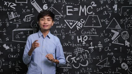 Wall Mural - Portrait of a smiling Asian woman math teacher set against a blackboard in a school classroom.